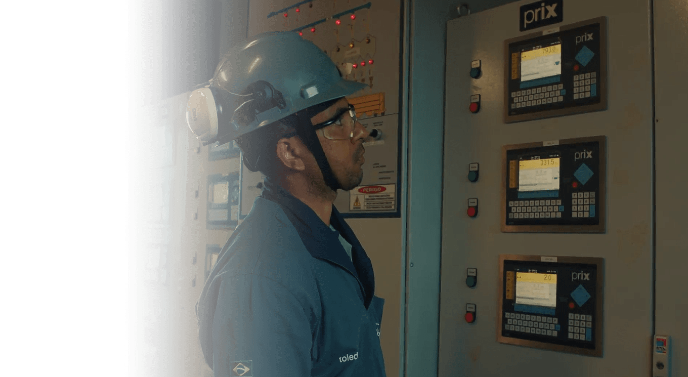 Profissional técnico observa painéis de controle industrial com tecnologia Prix da Toledo do Brasil.