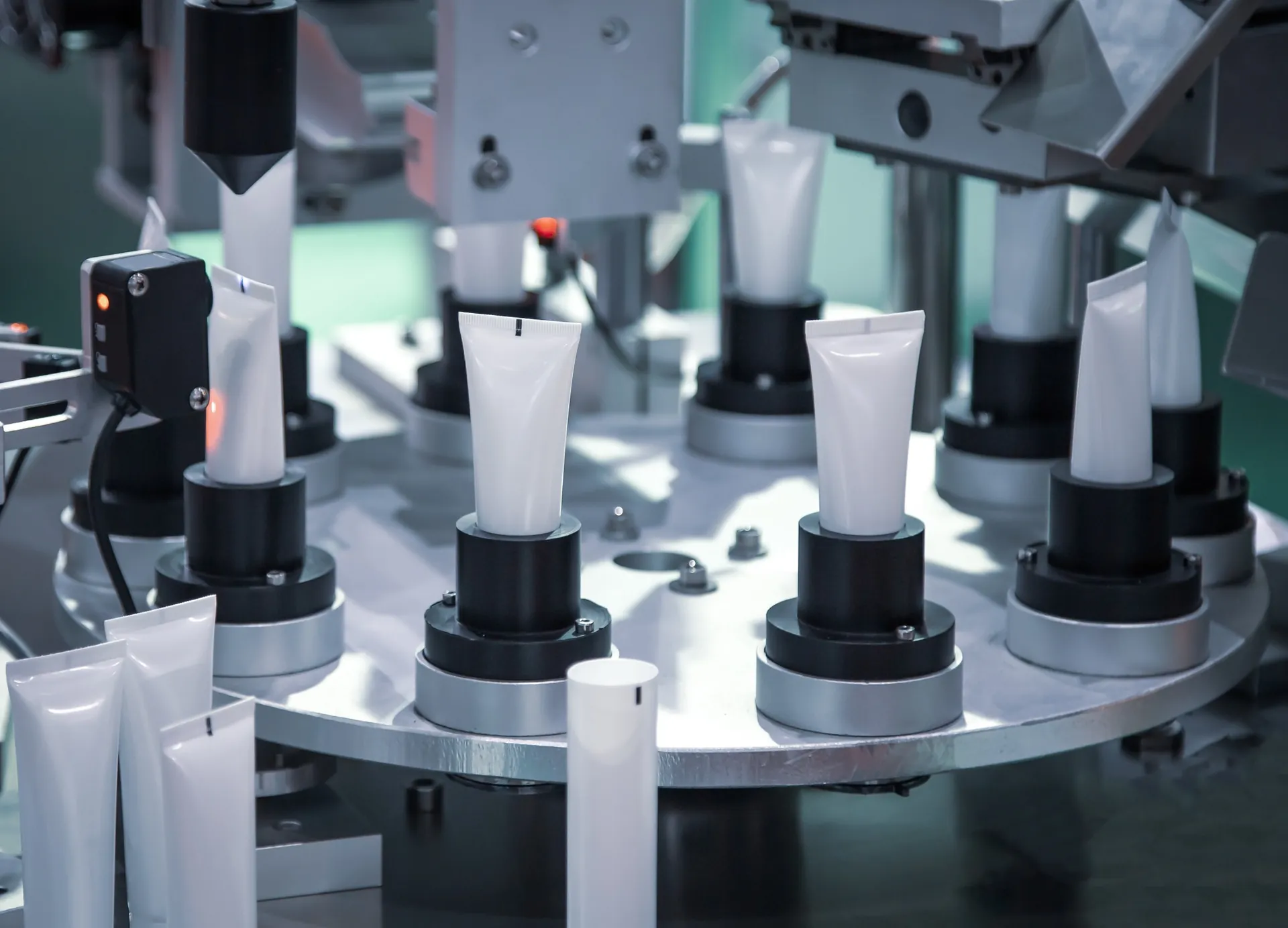Bisnagas brancas posicionadas em uma máquina industrial de envase.